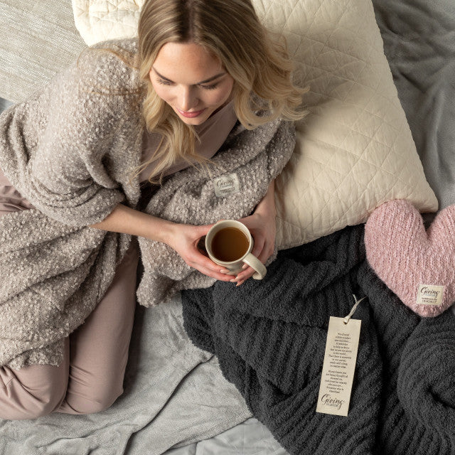 lady relaxing with tea next to Demdaco pink giving heart weighted pillow